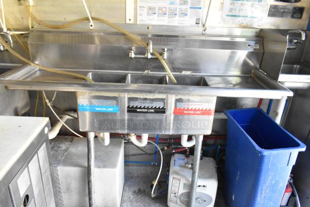 Stainless steel triple sink with labeled basins for wash, rinse, and sanitize in a mobile kitchen.
