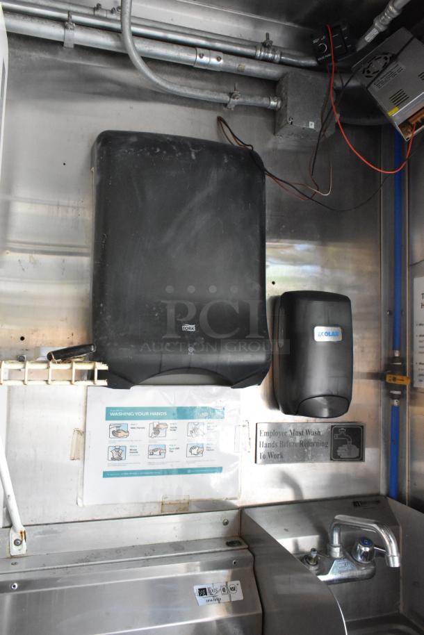Interior of a fully outfitted food trailer with a Tork paper towel dispenser and Ecolab soap dispenser mounted over a stainless steel sink.