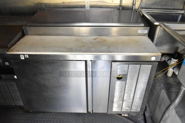 Stainless steel prep table with cooler storage, two hinged doors, and ventilation panel in food trailer. Good condition.