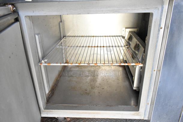 Interior view of a commercial food trailer cooler. Features a metal wire rack and visible fan components. Some signs of wear.