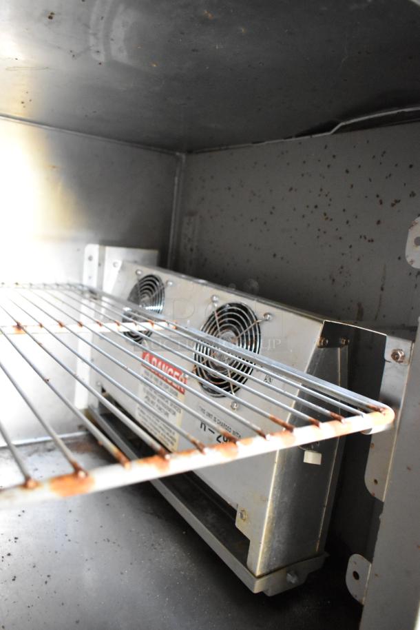 Interior view of food trailer's cooling unit with metal shelf, showing slight wear. Includes safety warning labels on unit.