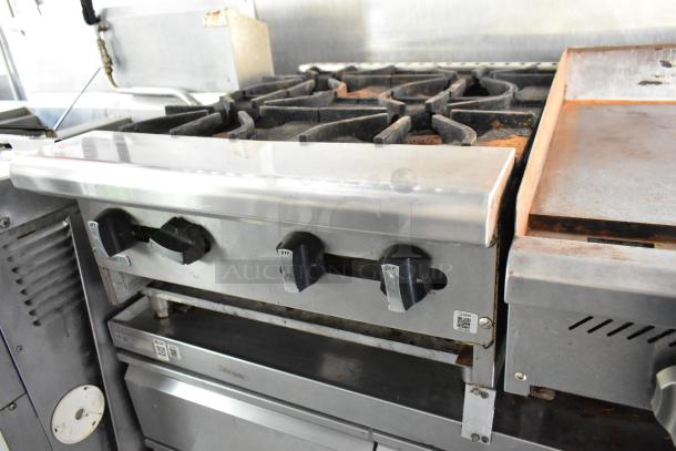 Stainless steel commercial range and flat top in a fully equipped food trailer kitchen, featuring control knobs and durable surfaces.