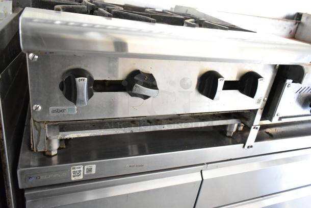 Stainless steel Asber range with control knobs, part of a fully equipped 2019 mobile kitchen trailer, featuring appliances for diverse cooking needs.