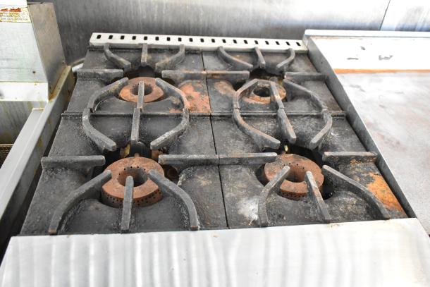 Four-burner stove in a food trailer, showing rust and wear, part of a fully outfitted mobile kitchen setup.