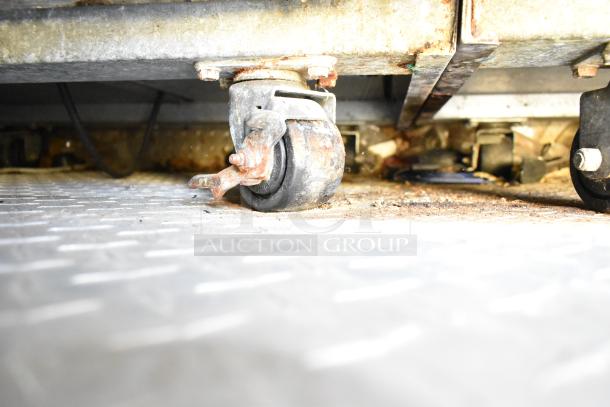 Underside view of a mobile kitchen showing a caster wheel on a diamond plate metal floor; some rust visible.
