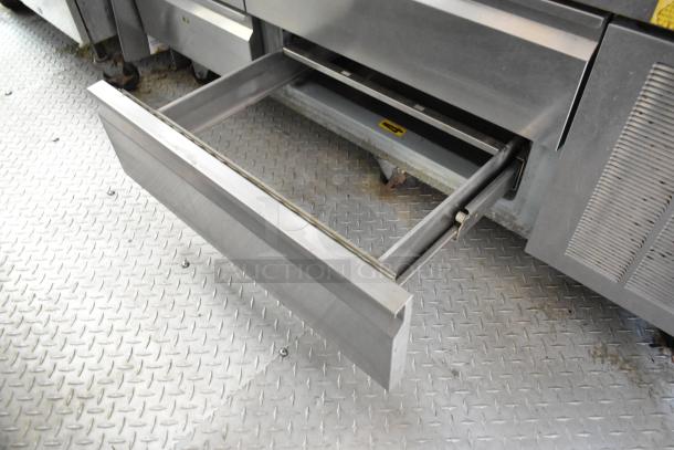 Stainless steel drawer unit, part of fully outfitted food trailer kitchen, on diamond plate flooring. Key for mobile kitchen setup.