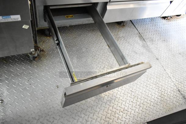 Interior of a food trailer showing a metal prep table drawer, diamond plate flooring, and industrial fixtures.