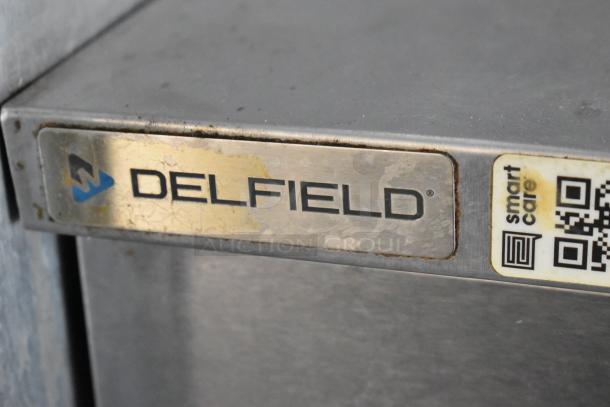 Close-up of a Delfield appliance label on a stainless steel surface, showing wear. Includes a QR code and "Smart Care" text.