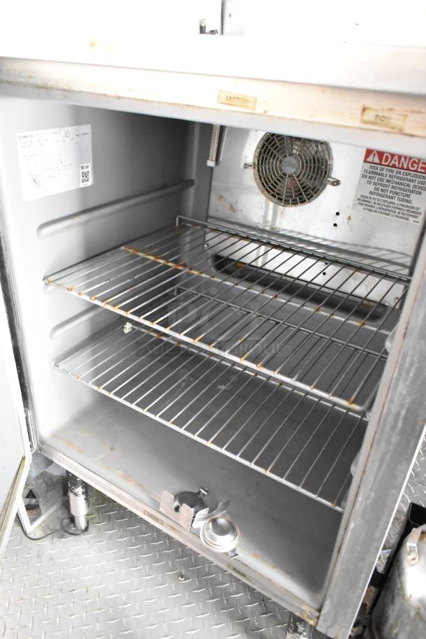 Interior view of a food trailer's appliance, featuring metal shelves, cooling fan, and safety warning labels. Clean condition.