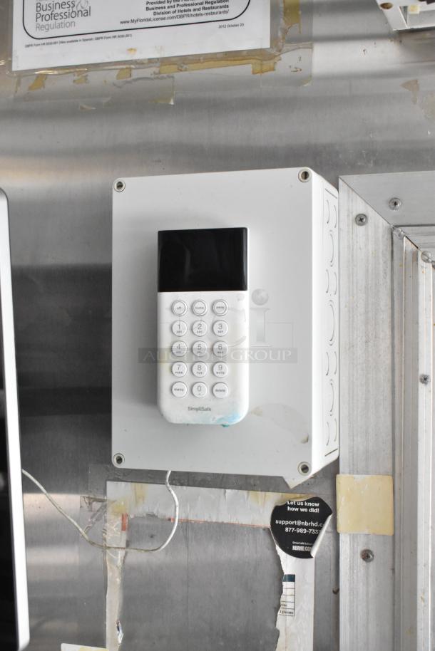 Alarm keypad mounted inside a mobile kitchen food trailer. SimpliSafe branding visible on the device.