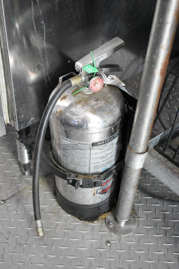 Fire extinguisher in a food trailer, equipped with instructional label and inspection tag, on a metal flooring.