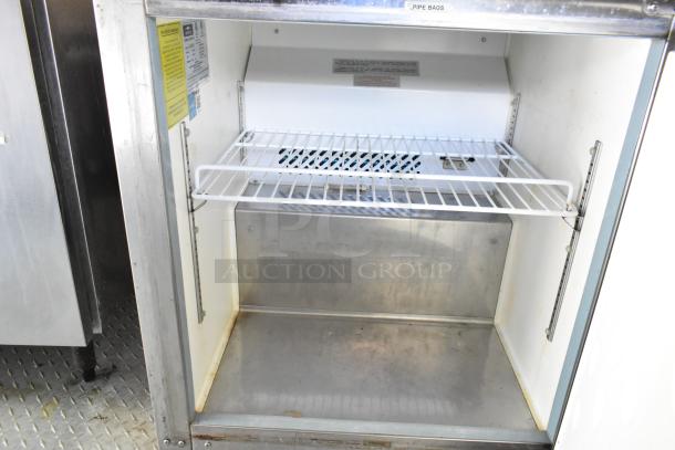 Open commercial food cooler with metal interior and adjustable wire shelf in stainless steel mobile kitchen trailer.