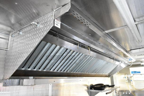 Stainless steel grease hood in new food trailer, featuring fryer, coolers, prep tables. Ideal for mobile kitchens.