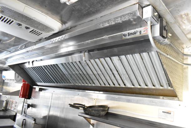 Stainless steel grease hood in a food trailer kitchen, featuring ventilation system and "No Smoking" sign.