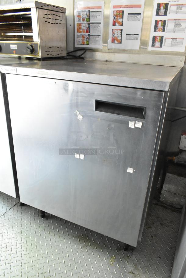 Stainless steel prep table with Delfield oven on top in a food trailer. Chef menus on wall behind.