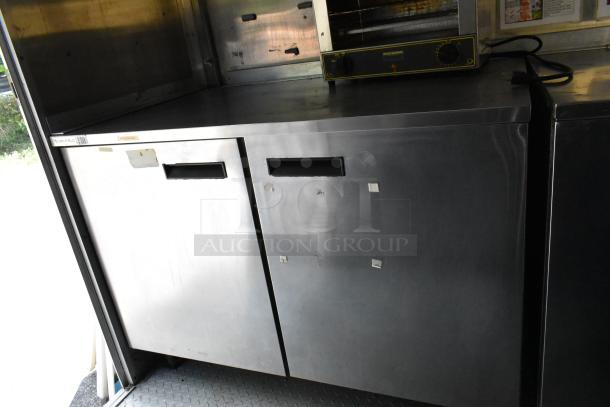 Stainless steel cooler unit in mobile kitchen, labeled Delfield with a smooth top surface and dual compartments.