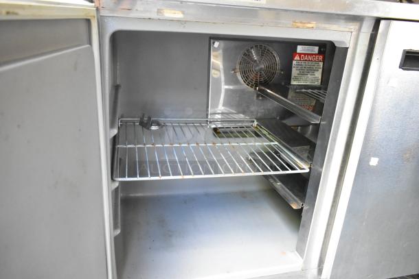 Interior of a fully outfitted mobile kitchen food trailer. Features open shelving and a warning label on the back panel.