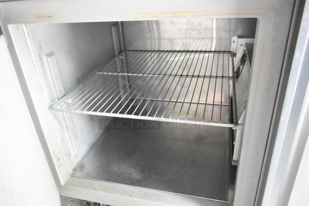 Interior view of a stainless steel cooler in a fully outfitted food trailer, showing a clean wire shelf and interior space.