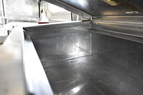 Interior view of a fully outfitted food trailer, showcasing a stainless steel prep table in pristine condition.