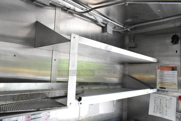 Interior view of a food trailer, showing stainless steel shelves, electrical wiring, and posted safety notices.