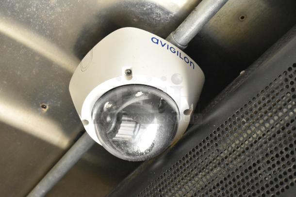 Ceiling-mounted Avigilon security camera in mobile kitchen, visible wiring, sturdy metal installation.