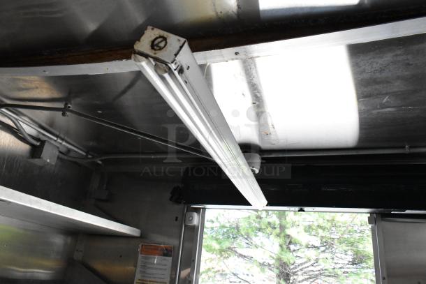 Interior view of a fully outfitted food trailer showing a ceiling-mounted fluorescent light fixture, wiring, and metallic surfaces.