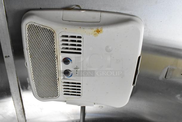 White overhead control panel in a food trailer, featuring dual knobs and ventilation grille, slightly discolored.