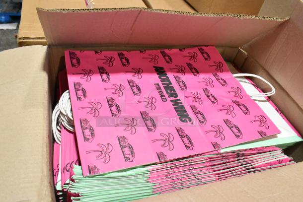Box of pink "Another Wing" paper handle bags with car and palm tree design, new condition, visible branding.