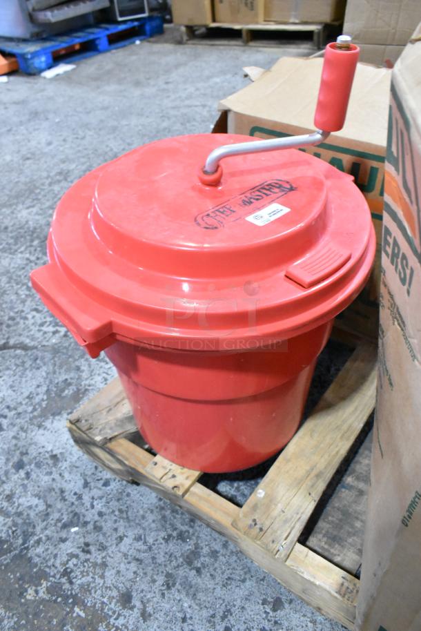 Red Chef Master salad spinner with crank handle on a wooden pallet. Lid features branding and a label.