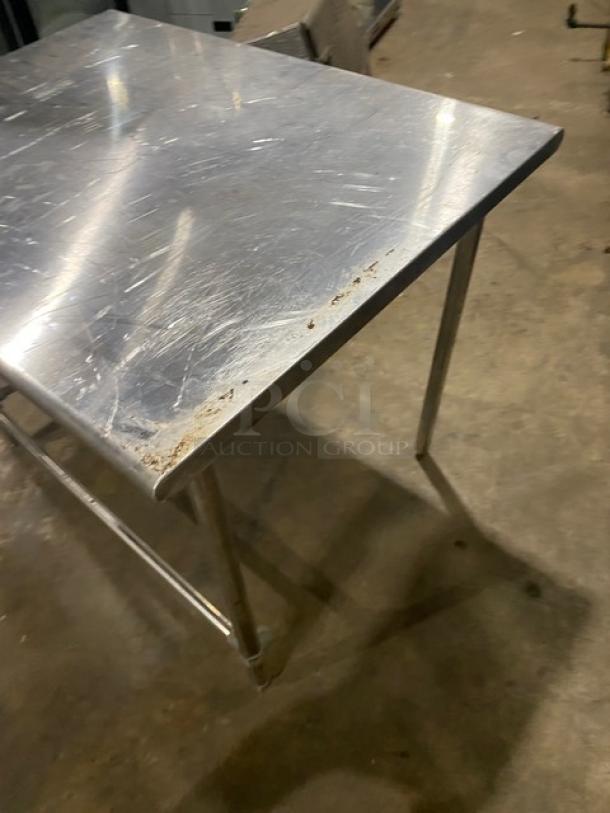 Commercial stainless steel open base worktop table with legs, showing surface wear and signs of use. Ideal for kitchen or workspace.