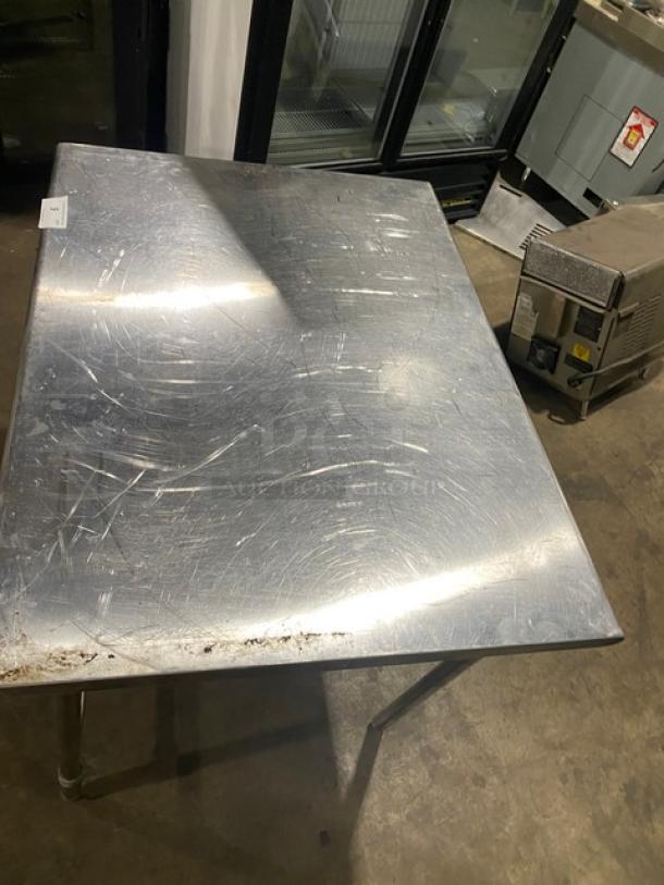 Commercial stainless steel worktop table with an open base and sturdy legs; features visible wear and scratches, indicating use.