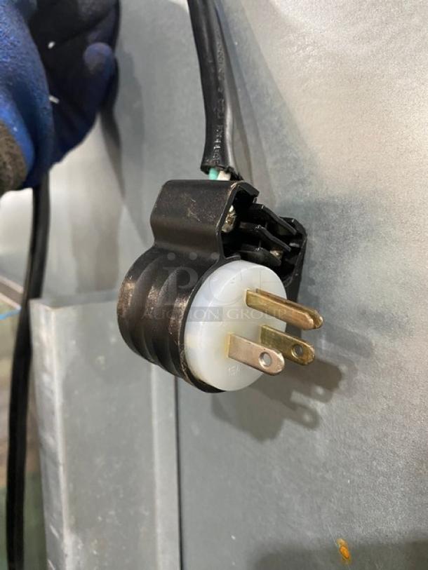 Three-pronged power plug of a Dukers D55AF commercial freezer, showing connection detail on a metallic background.