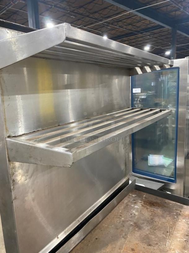 Jade Range stainless steel flat top range/oven combo with backsplash, double overhead shelf, and wired oven rack on casters.