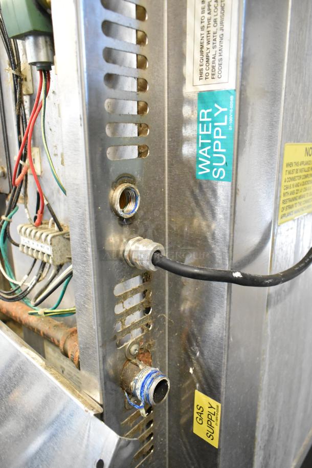 Baxter stainless steel commercial gas-powered mini rotating rack oven with visible water and gas supply labels, wiring, and connectors.