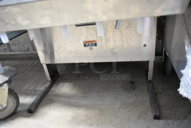 Bunn IMIX-5 stainless steel cappuccino machine underside, showing steel support legs and a "Hot Liquid" warning label.