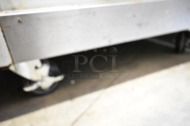 Blurry image showing part of a Traulsen G10010 cooler on a caster wheel.