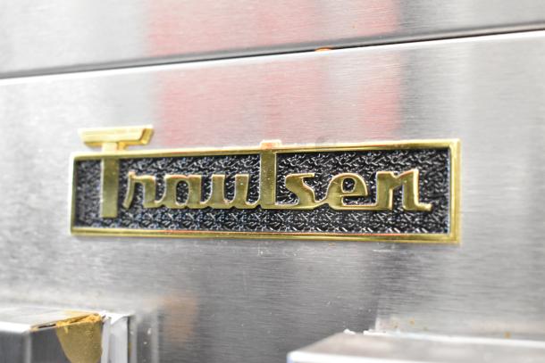 Traulsen G20010 stainless steel cooler badge, showing brand logo in gold on a textured black background.
