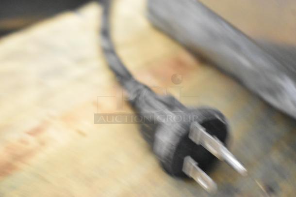 Blurry image showing the power cord with a plug of a Cadco Unox stainless steel convection oven. Electric powered, 208/240 volts.