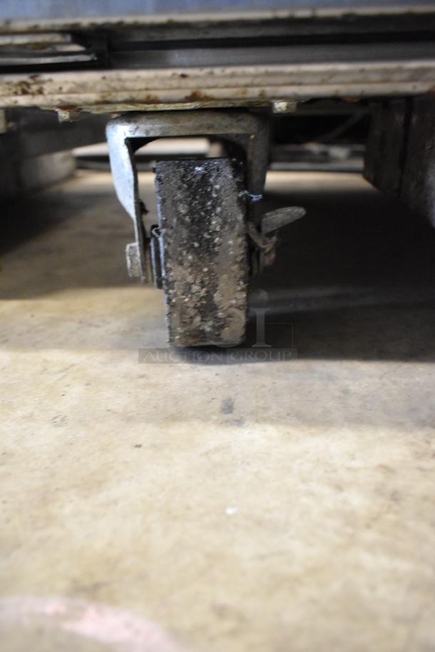 Close-up of a commercial caster wheel under a Moffat E89AMS Turbofan stainless steel convection oven, showing wear and dirt.