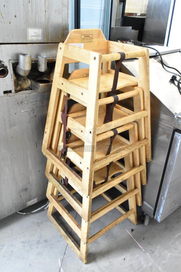 Four wooden high chairs, stackable design, natural finish, visible wear, includes safety straps, ideal for restaurants.