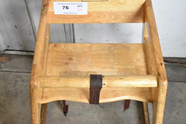 4 wooden high chairs with natural finish and visible wear. Features safety straps. Auction label indicates lot of four.