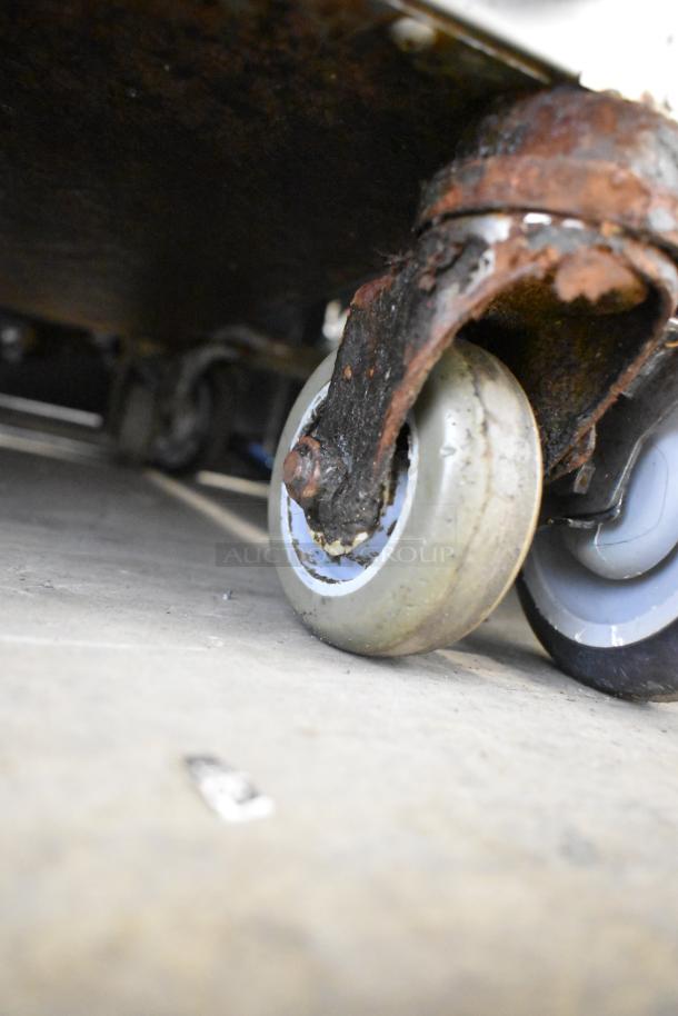 Close-up of worn commercial caster wheel on Alto Shaam 750-S stainless steel heated holding cabinet, showing rust and wear.