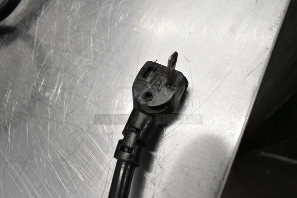 Black electrical plug for Alto Shaam 750-S heated cabinet, shown on the metal surface. Plug compatible with 120 volts, 1 phase.
