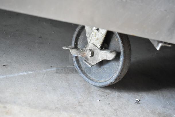 Close-up of a commercial caster wheel from a True TSSU-72-18-ST stainless steel pizza prep table. Shows wear.