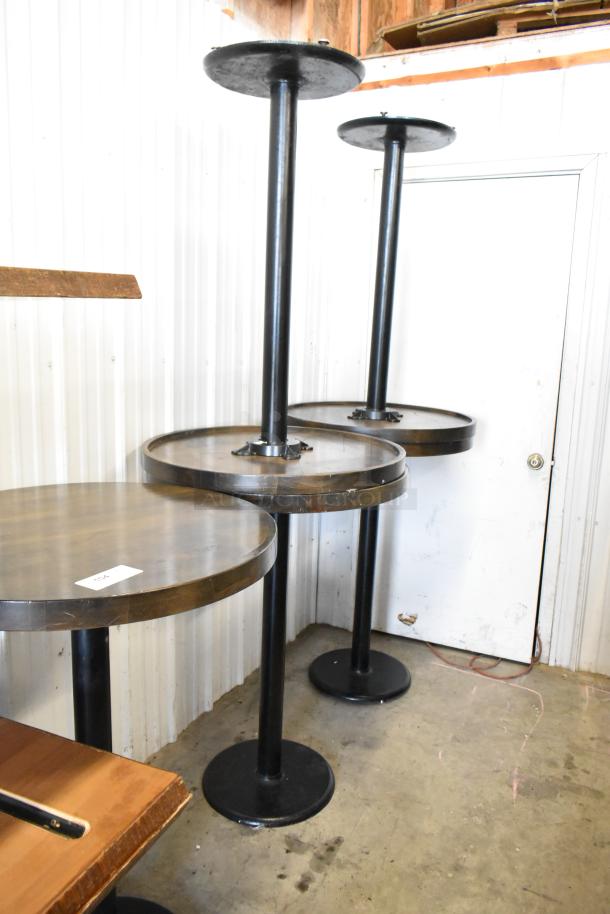 5 wooden round bar height tables with black metal bases, showing some wear. Includes visible auction tag with lot number.