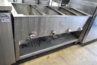 Stainless steel commercial gas-powered steam table with four burners and an under shelf, featuring control knobs and Yukon branding.