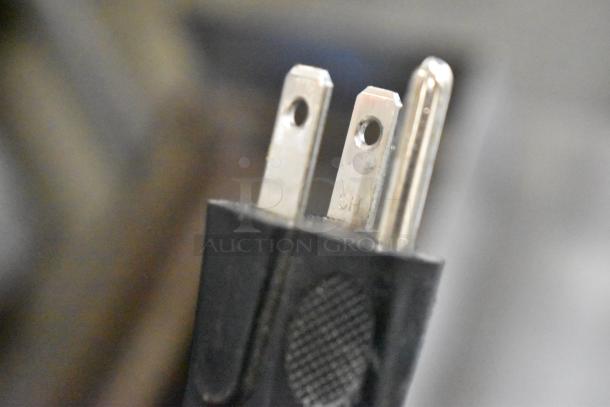 Close-up of a three-prong electrical plug with a black casing, showing minor wear. Focus on prongs and texture detail.