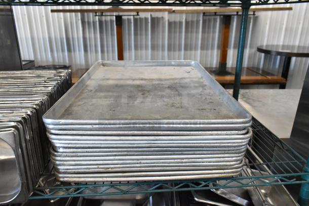 Stack of metal baking pans on a wire shelf, showing signs of wear. Part of a three-tier lot with stainless steel and poly bins.