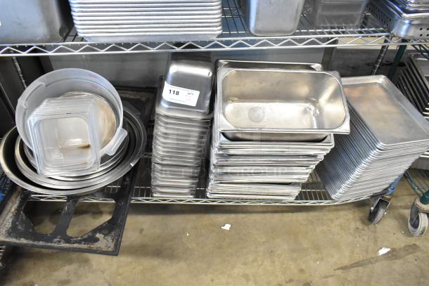 Stainless steel drop-in bins, metal baking pans, and bowls stacked on shelves. Auction tag reads "118 QTY T+".