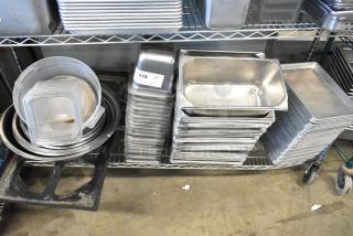 Stainless steel drop-in bins, metal baking pans, and bowls stacked on shelves. Auction tag reads "118 QTY T+".